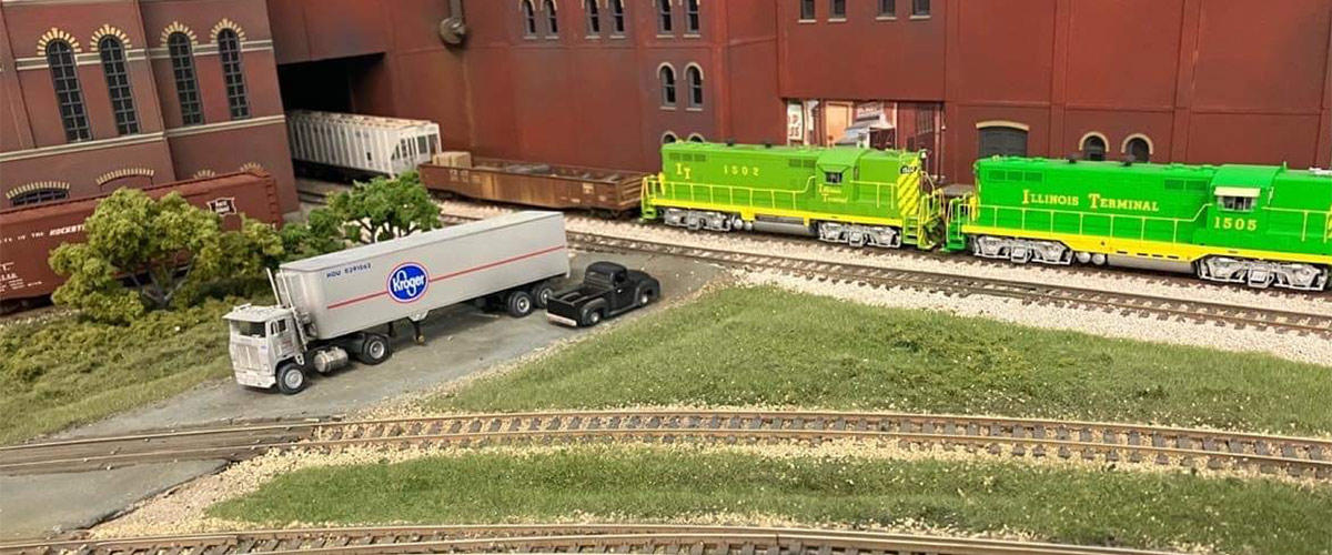 a model train and a model semi tractor trailer sitting in front of a model factory